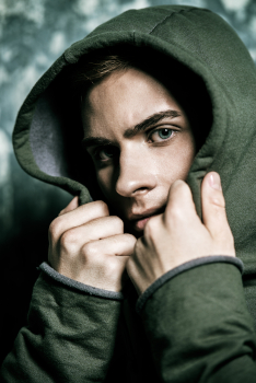 A sad male teen tucking his face into the hood of his sweatshirt