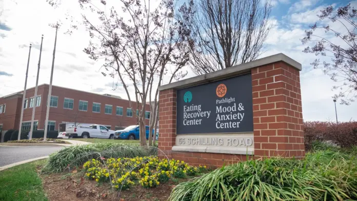 A brick sign with a green logo reads "Pathlight Mood & Anxiety Center." The sign is located in front of a large brick building with a parking lot and a few trees.