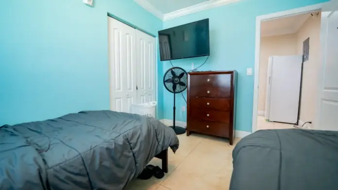 A bedroom at Reign Residential Treatment Center in Southwest Ranches, FL with two beds with blue comforters and a large TV